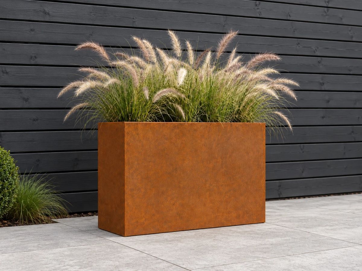 Rechthoekige cortenstaal plantenbak met siergras voor een antraciet houten schutting