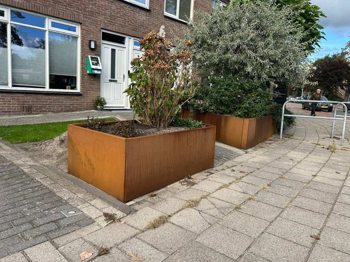 Grote cortenstalen plantenbakken in een voortuinopstelling